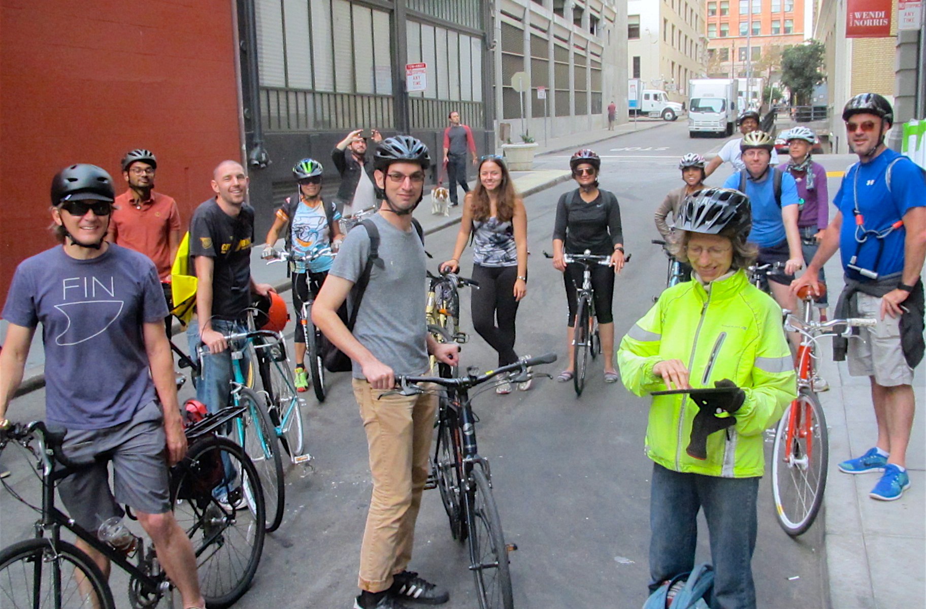 A group of smiling bicycle riders on an urban side street in San Francisco.