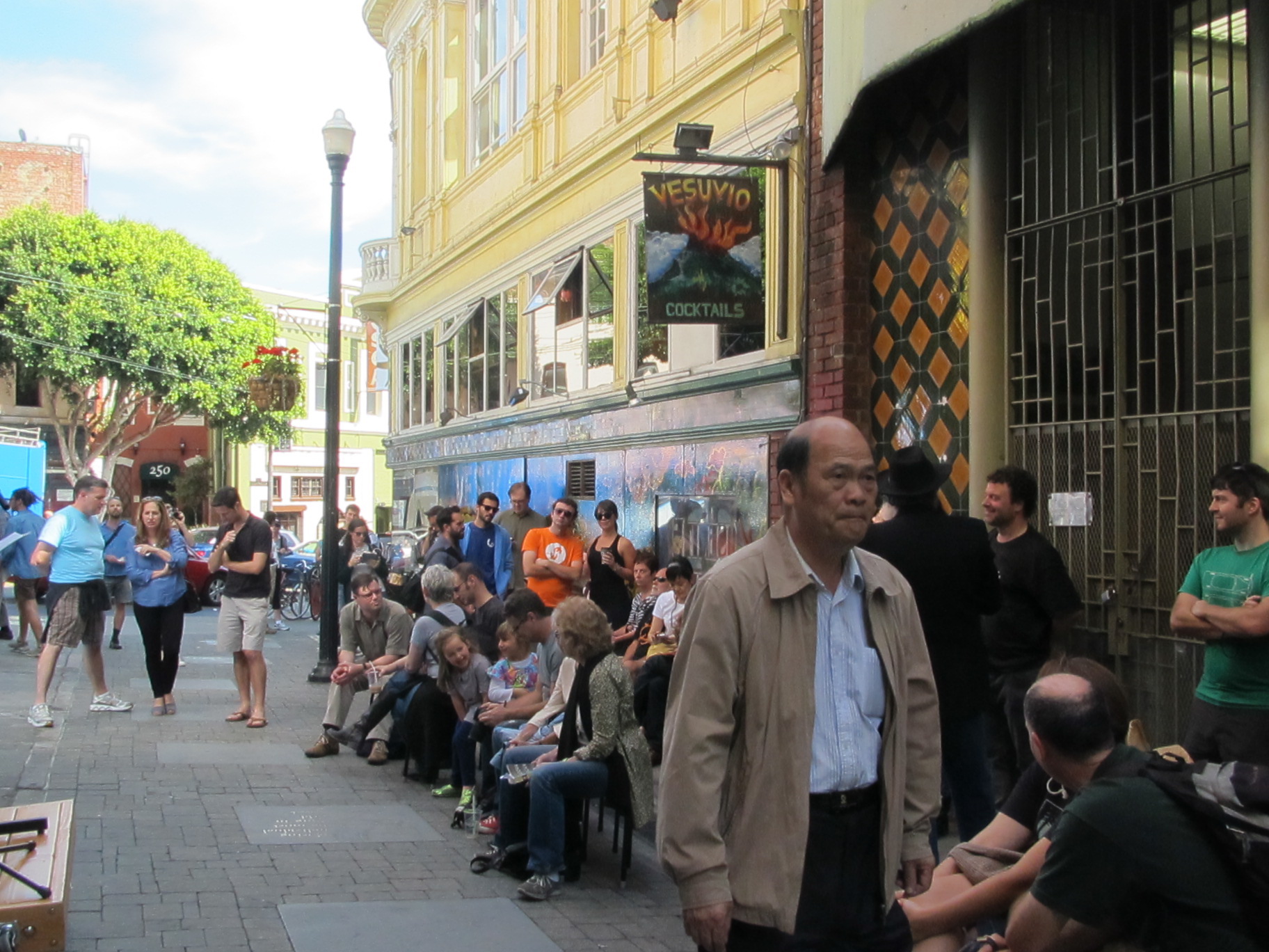 A gathering of people, some seated and some standing, on Jack Kerouac Alley outside of Vesuvio bar.