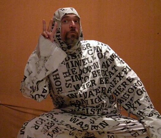 Lluis Valls a middle-aged man with a salt-and-pepper beard wearing a black and white tyvek suit printed on in large black letters that appear to be randomly chosen text