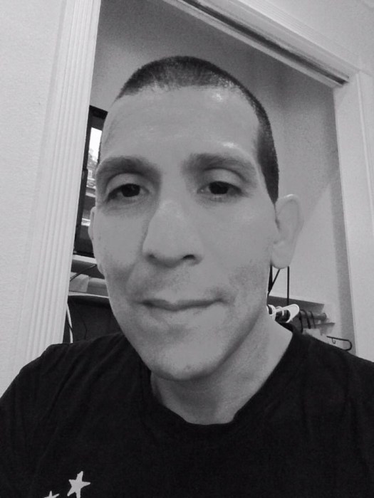Black and white closeup of Peter Griggs, a man with very close-cropped dark hair, smiling at the camera