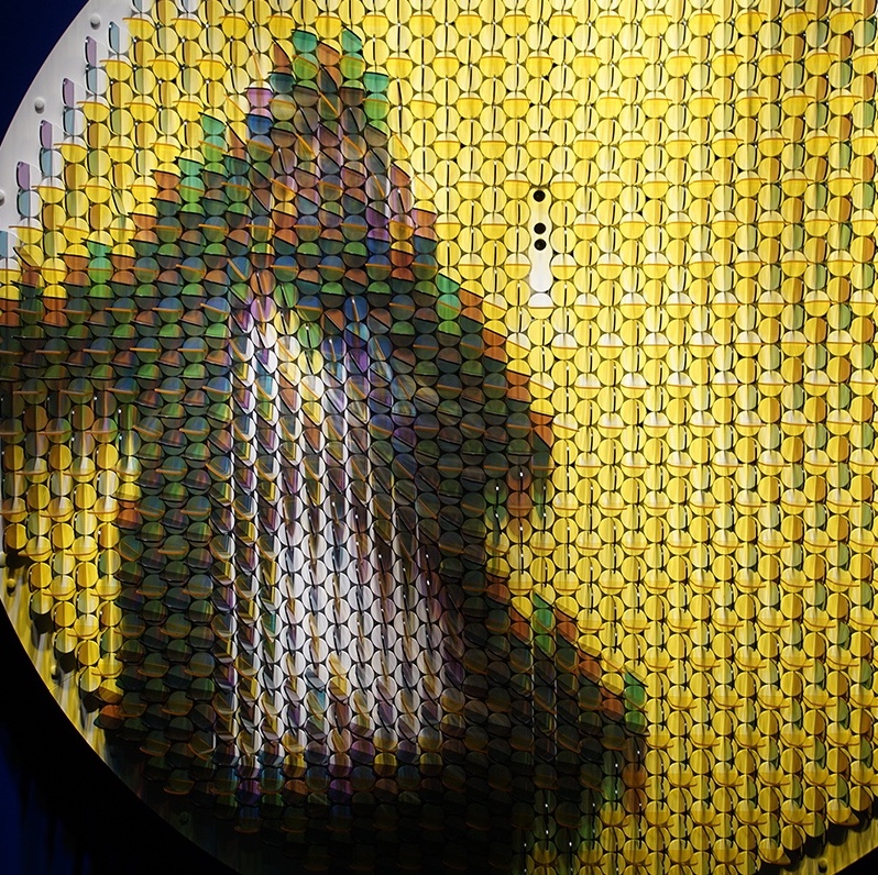 A silouette of Nicole Gluckstern taking a photo of herself reflected in the textured glass surface of an exhibit from the Exploratorium science museum